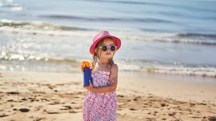 Immagine che rappresenta una bambina in spiaggia con in mano una crema solare